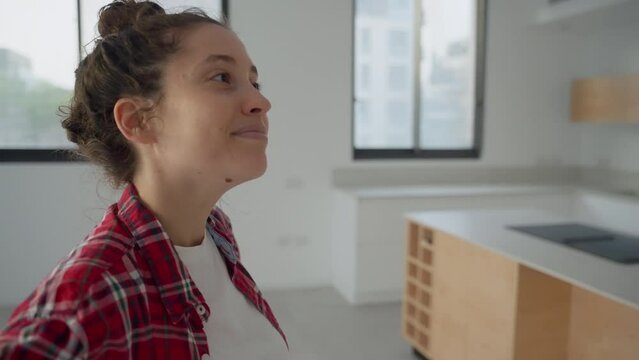 Interior designer or new home owner looking around the empty apartment. Smiling and envisioning the design and potential of her house. Brand new and empty blank walls and kitchen with no appliances