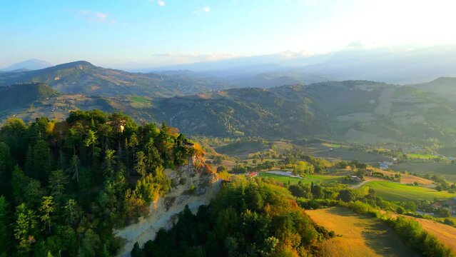 Gorgeous aerial truck right shot from Penna San Giovanni (MC), from the town's highest cliff filled with vegetation to the splendid underlying valleys with vivid green color, hills in the background