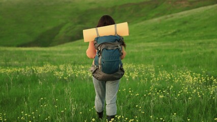 Free traveler woman walks through meadow with flowers in summer. Girl traveler travels along slope...