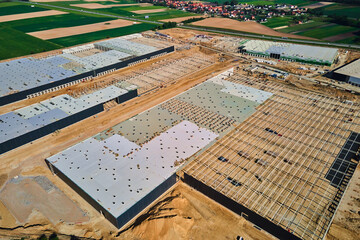 Aerial view of construction site with warehouse building under construction for storage. Assembling industrial building with steel frame structure and roof truss. Infrastructure for logistics