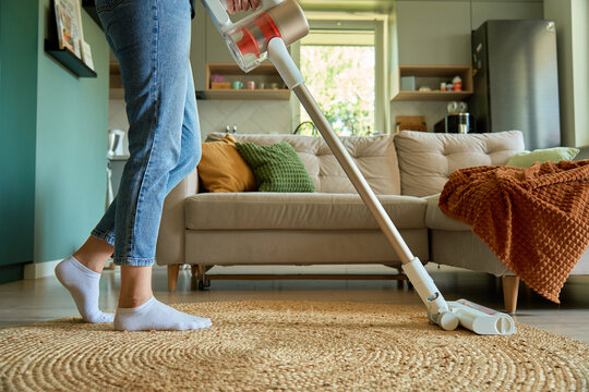 Woman is vacuuming floor of modern apartment living room, using portable cordless vacuum cleaner. Daily routine and household chores