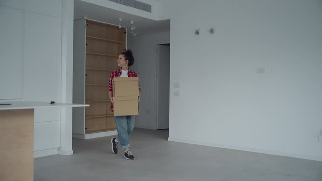 Entering their new home young woman and her cute dog walk inside with boxes. Happy and joyful to move into her apartment she carries cardboard boxes and calling her dog inside as they settle in