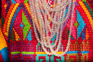A colorful necklace with a clear chain is displayed on a colorful background
