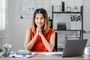 Professional Woman Working at Desk in Modern Office with Laptop and Documents, Smiling Confidently, Business Environment, Productivity, and Success Concept