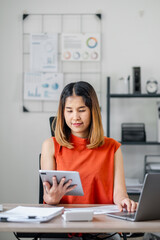 Young Professional Woman Working on Tablet and Laptop in Modern Office Setting with Charts and...