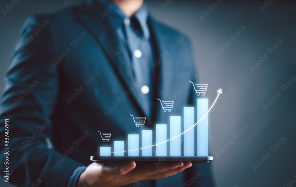 Wall mural Sale growth concept. Businessman showing graph of increase in sales volume with shopping cart on virtual screen for ecommerce growth.