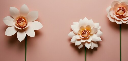 Two crafted paper flowers with intricate details, resembling a lotus and a rose, displayed on a soft pink background.