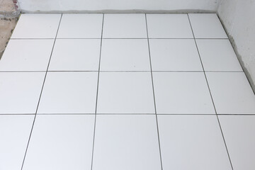 Tile floor under construction in perspective view by white square ceramic tile. Finishing material for interior, decoration, installation on concrete surface floor in bathroom, kitchen and shower room