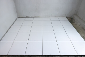 Fototapeta premium Tile floor under construction in perspective view by white square ceramic tile. Finishing material for interior, decoration, installation on concrete surface floor in bathroom, kitchen and shower room