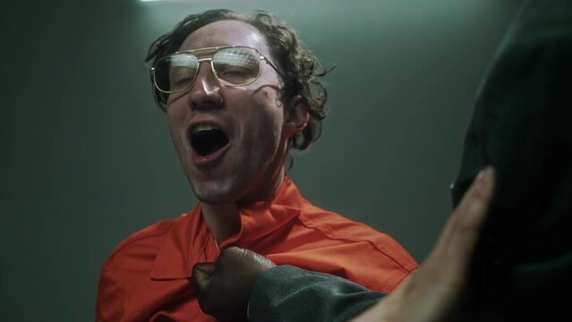 Close-up shot of hands of furious African American male police officer grabbing and shaking brazen Caucasian male murder suspect by throat during rough questioning, man laughing hysterically