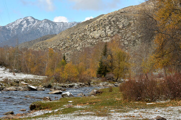 A beautiful winding river with rocky banks flows through the autumn valley in the mountains covered with the first snow.