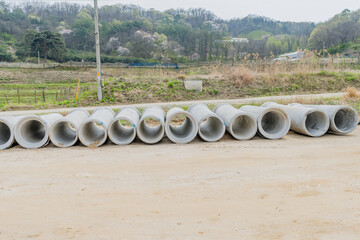 Row of concrete culvert pipes on ground at rural construction site.