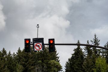 Traffic light on red on a stormy day, no left turn sign and traffic surveillance camera mounted with traffic signals
