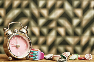 Golden toned image with pink alarm clock, buttons and scrunchy on the wooden table. Fashion theme...