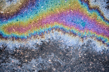 Droplets of gasoline and motor oil have accumulated on the blacktop, creating a striking abstract...