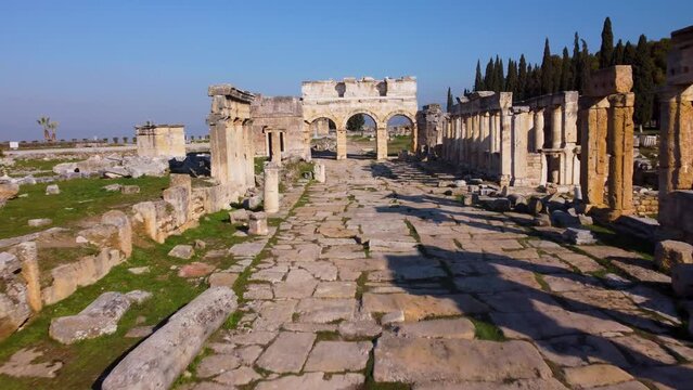 Tourist walks to Historic arched city gates to the ruins on Main Street promenade walkway. Ancient Roman, Greek and now Turkish city of Hierapolis. Pamukkale, Denizli, Turkey (T&uuml;rkiye) 4K