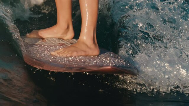 Close up of female wake surfer's feet on pink board surfing perfect shimmering wave on lake in slow motion