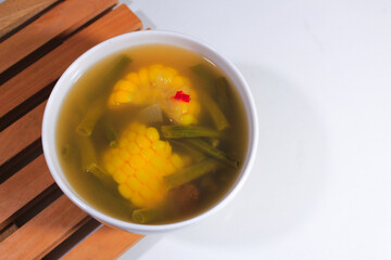 sweet and sour corn vegetable soup with porcelain bowl and wooden coaster