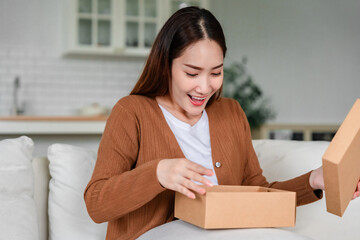 Happy young Asian woman opening delivery package at home. Beautiful female customer open box and...