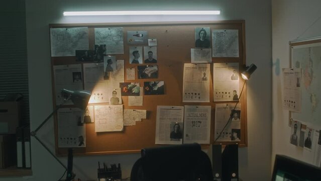 Zoom-in no people shot of pin board on wall at federal intelligence or law enforcement agency, with photos of suspects, APBs, maps, newspaper articles, crime scene photos, desk, chair