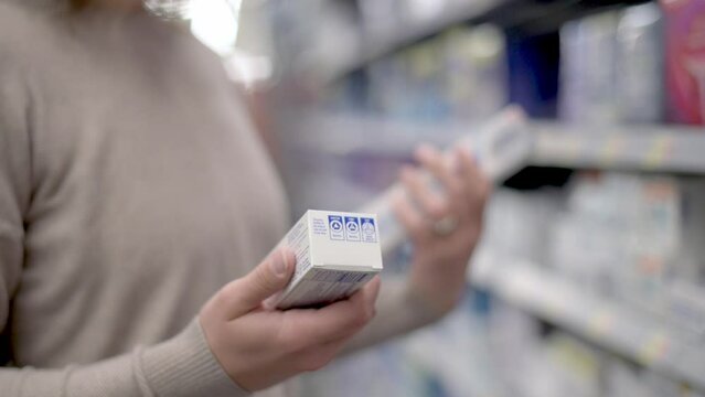 A woman examines two boxes of toothpaste in a store aisle, comparing them. The scene captures the act of decision-making in a retail environment.