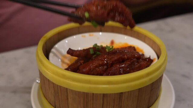 A person picks up a piece of chicken feet with chopsticks from the bamboo container.