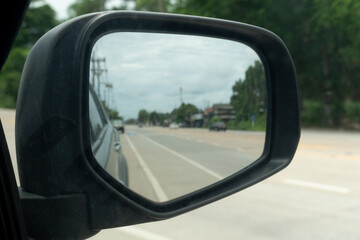 Obraz premium Inside view of mirrors wing. Rear view of a gray car with asphalt road and green trees with small city in the daytime. Clear traffic in rural areas.