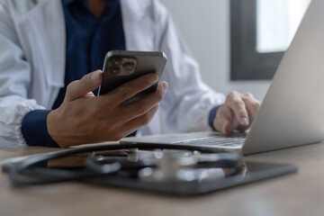 Fototapeta premium Doctor using mobile smartphone working on laptop computer in medical office Close the teleconference telemedicine
