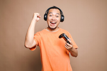 Happy Asian man playing video games rejoice victory isolated on beige background