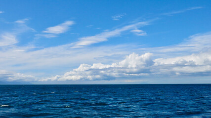 View of the blue sea and white clouds above the horizon. View of small waves on the sea surface and...
