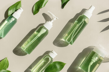 Pattern of transparent different bottles with green liquid and green leaves on beige, organic skin...