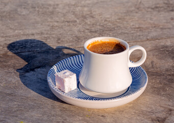 Traditional Turkish coffee in a white cup and blue and white saucer with a Turkish delight candy on a gray concrete table surface; copy space