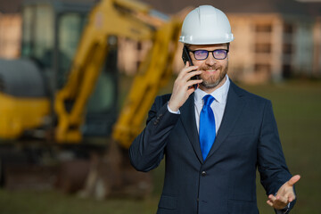 Construction builder investor. Man investor in front of construction site. Successful handsome man standing at modern home building construction. Portrait of midlle aged investor in suit and helmet.