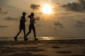 Asian Couple jogging and running outdoors sea sand beach. Sporty people wearing sportswear jogging. Male female athlete running during sunset on the beach. Workout exercise. Healthy and lifestyle.