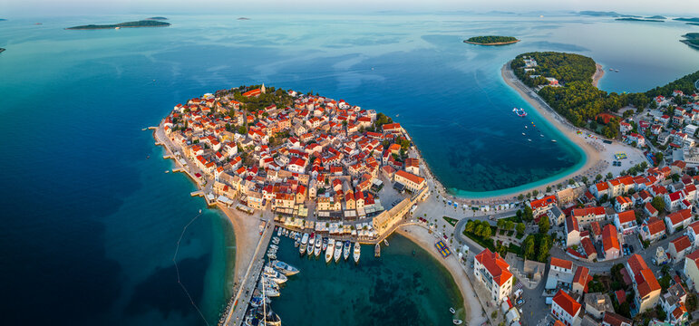 Primosten, Croatia - Aerial panoramic view of Primosten peninsula, St. George's Church and old town on a sunny summer morning in Dalmatia. Yacht marina, public beach at sunrise by the Adriatic sea