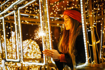 Woman holding sparkler night while celebrating Christmas outside. Dressed in a fur coat and a red...