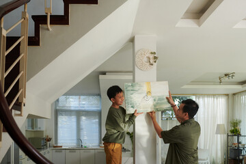 Boy helping father to hang picture on wall