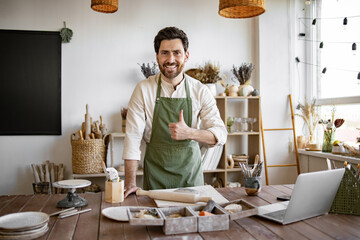 Concept of small business and trade in handmade products. Happy Caucasian bearded male potter making dishes from clay for online sales.