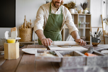 Process of making piece of pottery art in bright studio against background of shelves with...