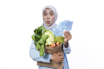 Young woman wear casual clothes hold brown paper bag with vegetable products and money isolated on white background studio portrait