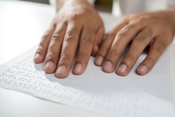 Hand of a blind person reading some braille text on page paper to learn. Finger of blind student...