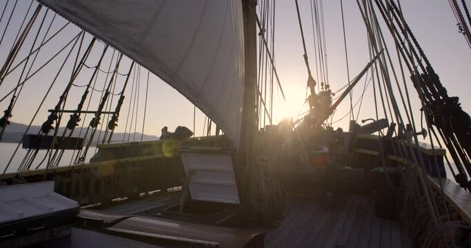 1700s sailing ship underway at sunrise. Static wide shot of bow. Sun burst causing lens flare across the bow.