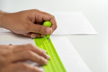 Close up Hand of a blind person writing some braille text on page paper. Young blind man using...