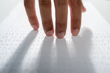 Hand of a blind person reading some braille text on page paper to learn. Finger of blind student touching the braille alphabet Code on sheet.