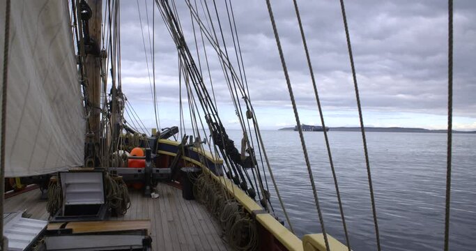 1700s sailing ship underway at sunrise. Cliffs and cargo ship off the bow. Static wide shot.