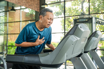Senior sporty person in sports uniform running on treadmill. Old man  he felt a pain in his chest held his hand and squeezed it. Mature Heart attack that needed treatment.