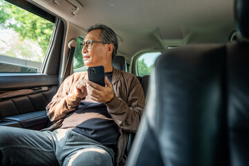 Relaxing moment of mature man sitting in car back seats using smartphone application on social media look out the window. Senior man happy in car traveling on the road to destination.