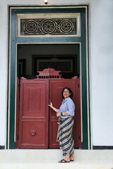 Woman standing in the front door of an old vintage Javanese architectural house © Simon