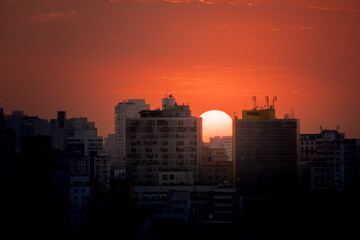Sun setting amidst buildings in the city of São Paulo and tinting the sky in a deep orange color