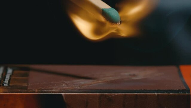 Green tipped matchstick strikes matchbox and ignites a flame in slow motion